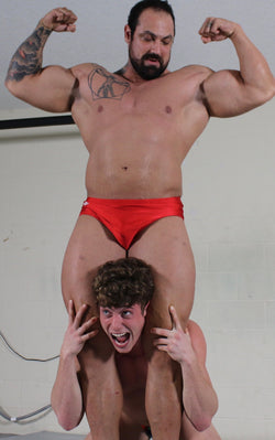 body builder flexing with small wrestler in a head scissors